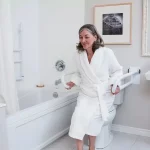 An elderly woman uses two toilet safety rails to transfer from the toilet.