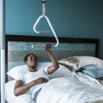 A woman using a SuperPole with a SuperTrapeze to pull herself to a sitting position while laying down in bed.