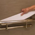 A hand placing the easily installed shelf unto the shelf of the Invisia Shampoo Shelf.