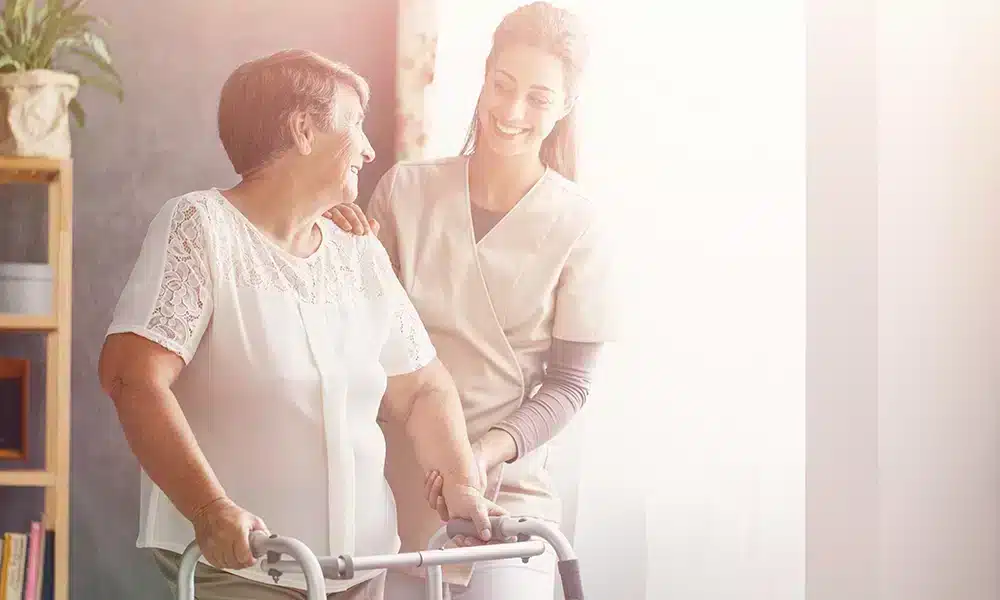 Caregiver helping an elderly woman move with a walker.