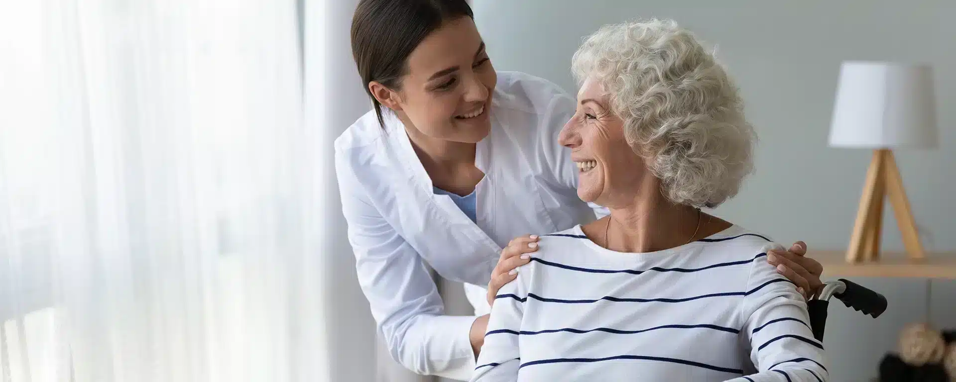 An occupational therapist with a senior woman in a wheelchair smiling.