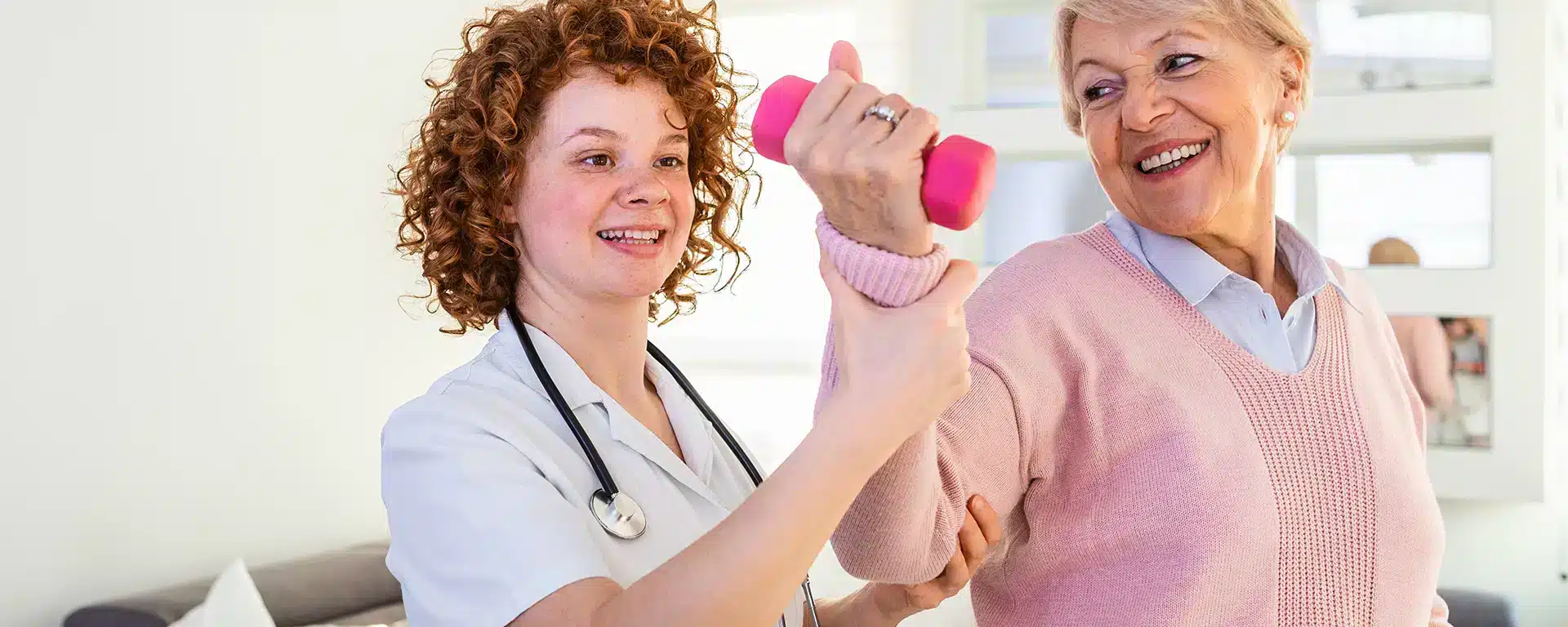 Occupational therapist helping a senior woman correctly lift a small dumbbell.